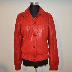 Röd retro / vintage äkta skinnjacka / vårjacka, Rock and blue, Strlk 40. NYSKICK. - Röd retro / vintage äkta skinnjacka i mjukt fint läder, från Rock n blue. Storlek: 40/M-L. Aldrig använd/nyskick. Svart mönstrat satinfoder, 2 fickor fram, 1 innerficka, stängs med knappar. Jackan är 67 cm lång. Plastfodral att förvara jackan i ingår.