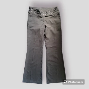 Lågmidjade svarta kostymbyxor - Ett par jättefina svarta kostymbyxor som är lågmidjade/midrise. Jättefina detaljer vid midjan, går ut vid benen. Fint skick.