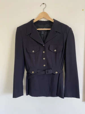 Kavaj från Escada  - Så fin kavaj från Escada!! Superfina detaljer med gröna knappar och bälte. Storlek 40.                                                                               Tyvärr saknas en knapp på ena armen. Men det syns knappt. Men därav priset. 