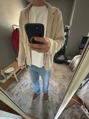 Beige stickad kofta med krage - Säljer en beige stickad kofta med krage och knäppning framtill. Koftan har en avslappnad passform, långa ärmar och är tillverkad i ett mjukt, ribbat material. Perfekt att slänga på över en t-shirt för en chill look.