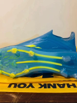 F50 Ice cold Precision ELITE LL - Säljer ett par blåa Adidas F50 fotbollsskor med gula detaljer och mönstrad sula. Elite väskan har blivit såld själv. Skorna har en strömlinjeformad design utan snörning och är tillverkade i syntetmaterial för lätt vikt och bra grepp på planen. Perfekta för dig som vill ha snabbhet och stil på fotbollsplanen.