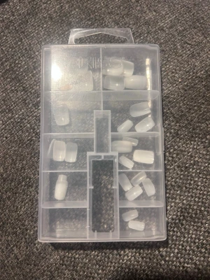 Vita press-on naglar i ask - Säljer ett set med vita press-on naglar i olika storlekar, levereras i en praktisk plastask med flera fack. Naglarna har en klassisk, lätt rundad form och är tillverkade i plast. Perfekt för dig som vill fixa snygga naglar snabbt och enkelt hemma.