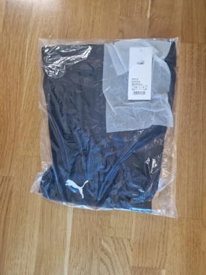 Svarta träningsshorts från Puma - Snygga svarta träningsshorts från Puma med klassisk vit logga på benet. Tillverkade i ett mjukt och funktionellt material som passar perfekt till träning eller sportaktiviteter. Shortsen har en enkel och stilren design.