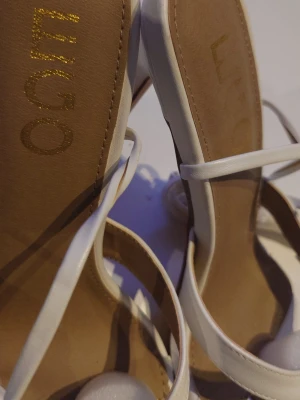 Vita pumps med snörning från Limo - Stilrena vita pumps från Limo med fyrkantig tå, tunna remmar och snörning runt ankeln. Skorna har hög klack och är tillverkade i ett slätt material som ger en elegant look. Perfekta för dig som vill sticka ut med trendiga detaljer.