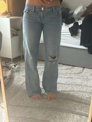 Ljusblå low baggy  jeans med hål - Säljer eftersom de inte kommit till användning, inprincip nya utan prislapp☺️.                                       Säljer ett par ljusblå raka jeans med hög midja och ett slitet hål på ena knät. Jeansen har klassisk femficksdesign och är gjorda i denim. Perfekta för en avslappnad och trendig look.
