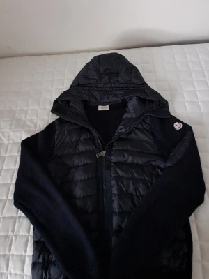 Mörkblå cardiganjacka från Moncler - Snygg mörkblå cardiganjacka från Moncler med quiltad front och huva. Jackan har stickade ärmar och muddar samt dragkedja framtill. Perfekt för lager på lager och har en sportig, modern look.