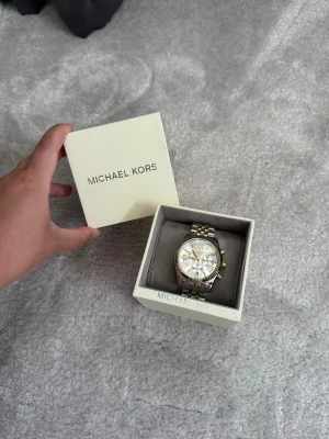 Michael Kors silver- och guldfärgad klocka MK5955 - Snygg klocka från Michael Kors i silver- och guldfärgad metall. Klockan har en rund urtavla med romerska siffror och flera små urtavlor. Länken är tvåfärgad och ger en lyxig känsla. Kommer i originalask. Inga defekter eller tecken på användning. 