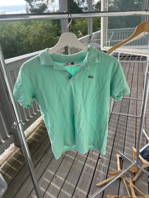 Turkos  pikétröja från Lacoste - Snygg mintgrön pikétröja från Lacoste med klassisk krage och korta ärmar. Tröjan har den ikoniska krokodilloggan broderad på bröstet och är gjord i mjukt bomullsmaterial. Perfekt för en avslappnad och stilren look.