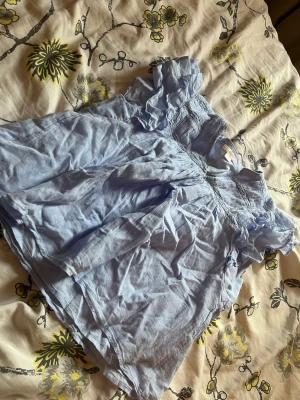 Ljusblå offshoulder blus Gina Tricot - Supersöt ljusblå blus från Gina Tricot med offshoulder-modell och volangdetaljer vid ärmarna. Blusen har smock upptill och är gjord i ett tunt, luftigt tyg som känns perfekt för sommaren. Passar dig som gillar en romantisk och avslappnad stil.