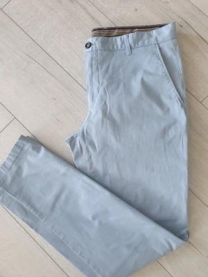 Ljusblå chinos från AC Sports - Snygga ljusblå chinos från AC Sports i storlek 50. Tillverkade i mjuk bomull med lite stretch för extra komfort. Klassisk passform med sidofickor och bälteshällor. Insidan har ett coolt mönstrat tyg som ger en unik touch.har två små fläckar se bild 5 därav låg pris. Har säjälv inte testat att bort det.