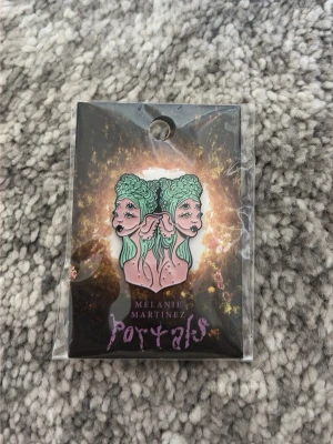 Melanie Martinez Portals Gemini pin - Unik emaljpin med tvillingmotiv från Melanie Martinez Portals-kollektion. Designen visar två ansikten med mintgrönt hår och rosa hud, inspirerat av zodiaken tvillingarna. Perfekt accessoar för dig som gillar alternativ stil och vill sticka ut.