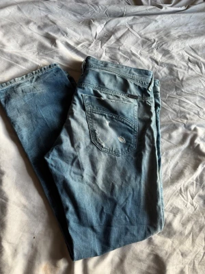 Diesel jeans - Säljer ett par ljusblå jeans från Diesel med slitningar och distressed detaljer på fickorna. Klassisk femficksmodell med snygg tvätt och Diesel Industry-märke på myntfickan. Perfekta för en avslappnad och trendig look. Passar w36/34