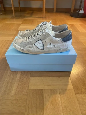 Beige Filip Modells med slitna detaljer  - Säljer ett par beige sneakers med slitna detaljer och svarta partier vid hälen. Skorna har vita snören med text och en unik patch på sidan. Låg modell med robust sula och vintage-look. Perfekta för dig som gillar streetstyle och en avslappnad vibe.