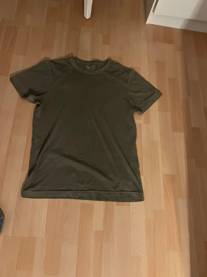 Olivgrön t-shirt från Dressmann - En enkel och stilren olivgrön t-shirt från Dressmann. T-shirten har rund halsringning och korta ärmar. Tillverkad i mjuk bomull som känns skön mot huden. Perfekt basplagg att matcha med jeans eller shorts.