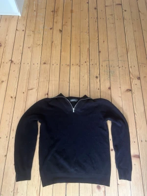 Dressman tröja - En svart långärmad tröja med halv dragkedja framtill och ribbade muddar vid ärmslut och nederkant. Enkel och stilren design som passar till det mesta. Perfekt för dig som gillar en clean look.