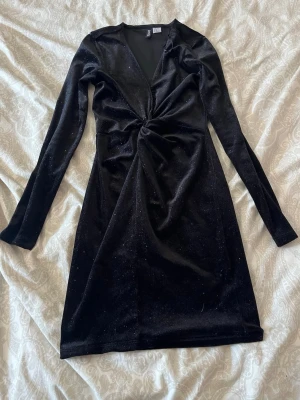 Svart glittrig klänning hm  XS - Snygg svart glittrig klänning från hm i storlek XS. Klänningen har lång ärm, v-ringning och twistad detalj framtill som ger en cool look. Perfekt för nyår och utekvällar. Obs går att sprätta upp fram vid v ringningen, då den är uppsydd där.🌸