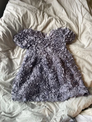 Ljuslila blommig klänning Minimarcket - Supersöt ljuslila klänning från Minimarket med 3D-blommor över hela plagget. Puffiga korta ärmar och rund halsringning. Perfekt för dig som vill sticka ut med en unik och lekfull look. ny pris 699kr priset är ej hugget j sren