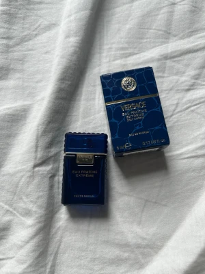 Versace Eau Fraîche Extrême parfym 5ml - Versace Eau Fraîche Extrême Eau de Parfum i en elegant, djupblå miniflaska på 5 ml. Flaskan har gulddetaljer och en stilren, rektangulär form med räfflade kanter. Kommer med matchande blå kartong med krokodilskinnsmönster och gulddetaljer.