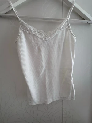 Vit ribbad linnetopp med spets från SHEIN - Snygg vit ribbad linnetopp från SHEIN med tunna axelband och spetsdetalj vid urringningen. Perfekt att styla till jeans eller kjol för en fräsch look. Materialet är mjukt och stretchigt för extra komfort.