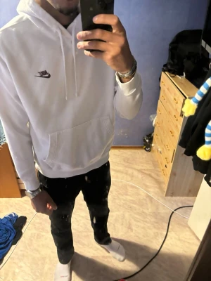 Vit hoodie från Nike med logga - Säljer en clean vit hoodie från Nike med den klassiska swoosh-loggan broderad på bröstet. Hoodien har huva med dragsnören och en stor magficka framtill. Perfekt för dig som gillar enkel och stilren streetwear.