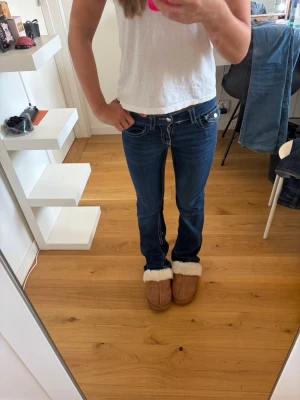 Mörkblåa bootcut jeans - Mörkblåa bootcut jeans från gina tricot i storlek 152. Använda men i fint skick. Sydd med vit söm och knappar på bakfickorna som går att stänga och öppna. Går att spänna vid höfterna.