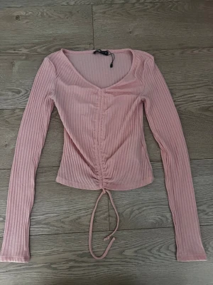 Rosa ribbad topp med snörning - Trendig rosa långärmad topp med ribbad struktur och v-ringning. Toppen har snörning framtill som kan justeras.