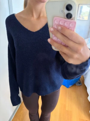 Mörkblå stickad tröja Vero Moda - Mysig mörkblå stickad tröja från Vero Moda med v-ringning och avslappnad passform. Tröjan har långa ärmar och är tillverkad i ett mjukt, lite luddigt material som känns skönt mot huden. Perfekt att slänga på sig när det är kyligt ute.