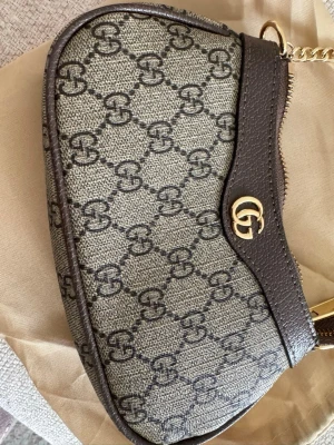 GG Axelväska - 🤎 Exklusiv Axelväska 🤎  ✅ Elegant och stilren design ✨ ✅ Rymlig och praktisk för dina viktigaste saker 📱💳🔑 ✅ Guldfärgade detaljer för en lyxig känsla ✨ ✅ Justerbar axelrem för maximal komfort 👌 ✅ Perfekt till både vardag och fest 👜 ✅ Tidlös design som passar alla outfits 🤎  ✨ En exklusiv axelväska med en klassisk design och stilrena detaljer. Den är både praktisk och elegant – perfekt för dig som vill bära med dig det viktigaste samtidigt som du kompletterar din outfit med en lyxig känsla.