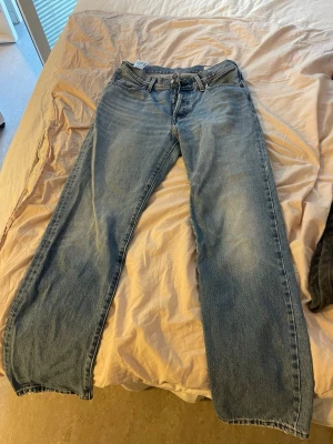 Blå raka jeans från Levi's - Klassiska blå Levi's jeans med rak passform och fem fickor. Jeansen har en ljus tvätt och tydliga sömmar, samt den ikoniska röda Levi's-lappen på bakfickan. Tillverkade i slitstark denim med bälteshällor och knappgylf.