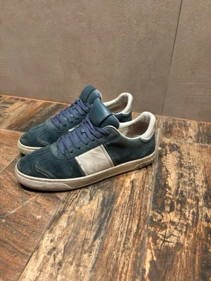 Blå sneakers med vit detalj - Blåa Valentino Flycrews. Skorna är använda men har mycket kvar att ge. 6 spikar är borta, 3 st på varje. Skorna är lite smutsiga men kan lätt tvättas bort.