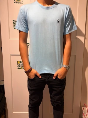 Ljusblå Ralph lauren T-shirt  - Snygg ljusblå t-shirt med rund hals och korta ärmar. T-shirten har en liten broderad logga på bröstet och är gjord i mjuk bomull som känns skön mot huden. Perfekt till jeans eller shorts för en clean och enkel stil. Xs/s