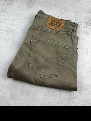 Olivgröna Levi's jeans raka ben 501, 32/32  - Snygga olivgröna jeans från Levi's med klassisk femficksdesign och raka ben. Jeansen har en patch med Levi's-logga bak i midjan och är tillverkade i ett slitstarkt bomullstyg. Perfekta för en avslappnad och trendig look.