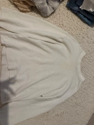 Vit stickad tröja från 157 - Klassisk vit stickad tröja från 157 med rund halsringning och ribbade muddar vid ärmslut och nederkant. Tröjan har en enkel och clean design som passar till det mesta. Perfekt för lager på lager och riktigt skön att ha på sig.