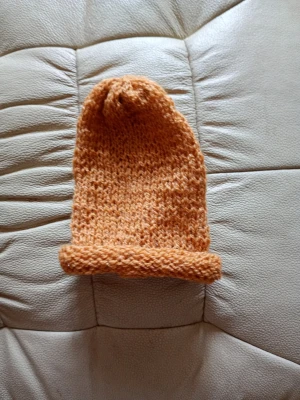 Handstickad orange mössa - Mysig handstickad mössa i varm orange färg. Mössan har en enkel, rak form med uppvikt kant och är gjord i tunt garn som ger en skön och avslappnad look. Perfekt för kalla dagar när du vill ha något unikt och bekvämt. Lite guldbrunorange.