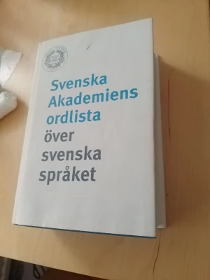 Svenska Akademiens ordlista - Svenska Akademiens ordlista över svenska språket är en klassisk bok med vit hård pärm och tydlig text i blått och grått. Perfekt för dig som vill ha koll på stavning och betydelser i svenska språket.
