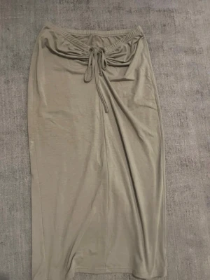 Beige långkjol med snörning - Stilren beige långkjol med elastisk midja och snörning framtill. Kjolen har en rak passform och en liten slits baktill för extra rörelsefrihet. Tillverkad i ett mjukt och stretchigt material som känns bekvämt mot huden.
