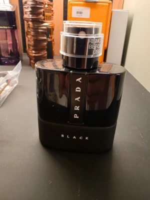 Prada Black parfym helt full - Snygg parfymflaska från Prada i modellen Black. Flaskan är svart med en stilren, modern design och har tydlig logga framtill. Lock i transparent plast med text. Perfekt för dig som gillar exklusiva dofter och vill ha en elegant flaska på hyllan.
