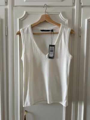 Vit ribbad linnetopp med v-ringning - Snygg vit ribbad linnetopp med djup v-ringning från Vero Moda, modellen heter VMCHLOE. Toppen har clean, enkel design som passar perfekt till jeans eller kjol. Materialet är mjukt och stretchigt. Helt oanvänd med alla lappar kvar! Nypris är 189 kr.