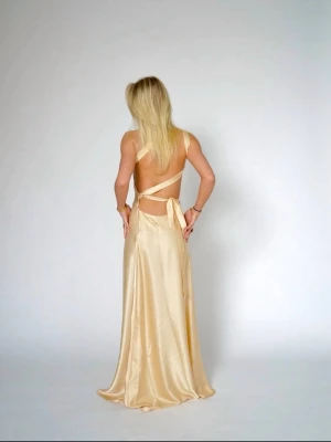 Handgjord ljusgul långklänning i satin - Elegant långklänning i champagnefärgad satin med oneshoulder och öppen rygg. Klänningen har omlottdetalj och knyt i ryggen för en snygg siluett. Klänningen är köpt från By Stina (svensk tjej som gör klänningarna själv). Nypris 1 595💛💛💛Klänningen är använd endast en gång! Kontakta mig vid intresse! 