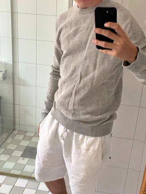  stickad tröja Jack & Jones - Snygg ljusgrå stickad tröja från Jack & Jones med rund halsringning och ribbade muddar vid ärmslut och nederkant. Tröjan har en diskret struktur i stickningen och passar perfekt till både jeans och shorts.