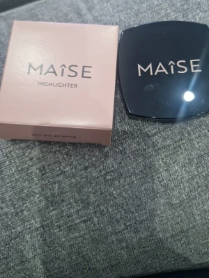 MAISE Highlighter i guldig nyans - Highlighter från MAISE i en snygg guldig nyans. Kommer i en stilren svart kompakt dosa med spegel och tillhörande rosa förpackning. Perfekt för att ge glow till ansiktet och framhäva dina drag.