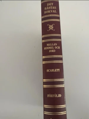 Det Bästas Bokval: Mellan himmel och jord - En tjock bok med hård, vinröd pärm och guldfärgad text på ryggen. Innehåller titlarna 'Mellan himmel och jord', 'Scarlett' och 'Förföljd'. Perfekt för dig som gillar klassisk skönlitteratur och samlingsvolymer.