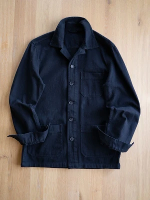 Black Chore Jacket, size M - Stilren svart overshirt i kraftigt bomullstyg med klassisk krage och fem knappar framtill. Tre utanpåliggande fickor, en på bröstet och två nedtill. Perfekt lager på lager-plagg för en avslappnad look.