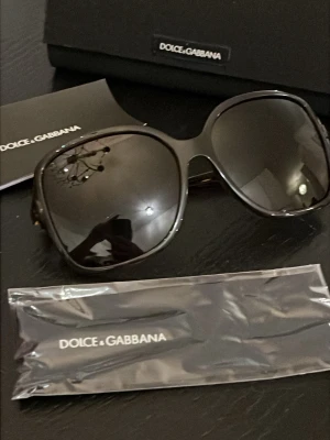 ÄKTA Svarta solglasögon Dolce & Gabbana - Stilrena svarta solglasögon från Dolce & Gabbana med stora, fyrkantiga bågar och mörka linser. Kommer med originalfodral och putsduk. Äkthetsgarantin följer med och serienummer syns på bilderna..