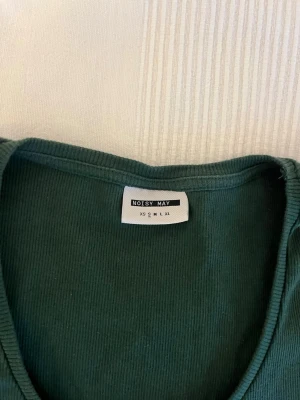 3-pack tröjor - Mörkgrön ribbad t-shirt från Noisy May med rund halsringning och korta ärmar. T-shirten har en slim passform och är tillverkad i mjuk bomull, perfekt för en enkel och stilren look. Vit tunn långärmad tröja ifrån H&M i storlek S. Svart långärmad ribbad tröja från Nelly i storlek S. 