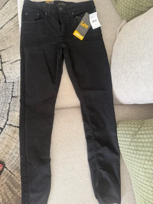 Svarta skinny jeans från Lee - Säljer ett par svarta skinny jeans från Lee med klassisk femficksdesign och smal passform. Jeansen har normal midja och är tillverkade i stretchigt material för extra komfort. Perfekta för dig som gillar en tajt look och vill ha ett par stilrena jeans.