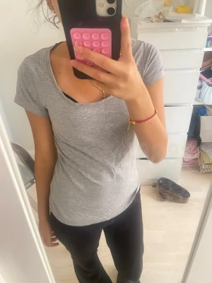 Grå basic t-shirt med rund hals - En enkel och stilren grå t-shirt med rund halsringning och korta ärmar. Perfekt till jeans eller tights för en avslappnad look. Tillverkad i mjukt bomullsmaterial som känns skönt mot huden.