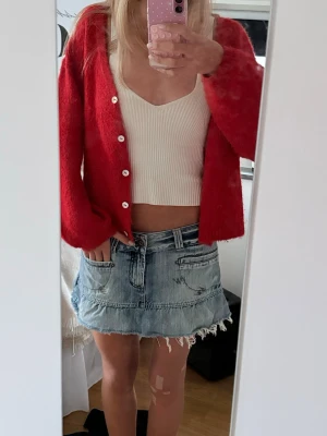 Blå jeanskjol med rå kant - Säljer en kort blå jeanskjol med rå, fransig kant och slitna detaljer. Kjolen har två framfickor och en avslappnad passform som ger en cool och trendig look. Perfekt för dig som gillar en casual och edgy stil.
