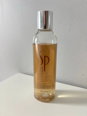 Wella SP Luxe Oil Keratin Protect - Wella SP Luxe Oil Keratin Protect Shampoo är ett lyxigt, lätt schampo som rengör håret skonsamt och ger skydd med keratin. Kommer i en genomskinlig plastflaska med silverfärgat lock och rymmer 200 ml. Perfekt för dig som vill ha ett vårdande och återuppbyggande schampo. Endast testad.