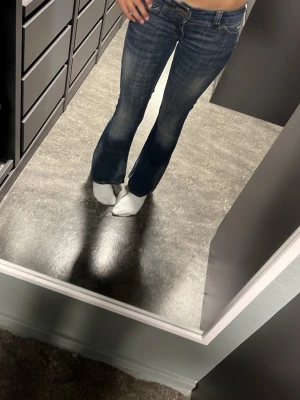 Mörkblå bootcut jeans med låg midja - Säljer ett par mörkblå bootcut jeans med låg midja och klassiska fem fickor. Jeansen har snygga slitningar och kontrastsömmar som ger en trendig look. Perfekta för dig som gillar en avslappnad men ändå stilsäker stil.